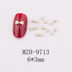Détail de mini nœuds dorés pour ongles avec perles sur une manucure rouge vif