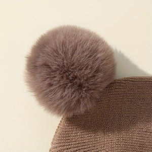 Dettaglio del cappello in maglia marrone per neonati con pompon in ecopelliccia