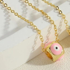 Detail of pink enamel evil eye pendant on a gold chain over a white stone base
