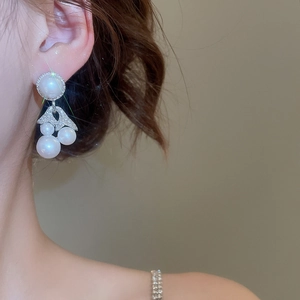 Elegant pearl earrings with sparkling fishtail design worn on a model's ear