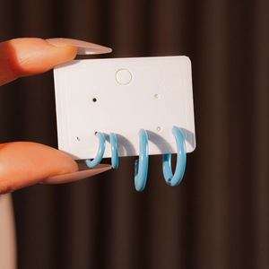 Close-up of two pairs of blue resin C-shaped hoop earrings on a display card