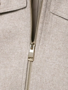 Close-up of polished gold zipper detail on premium light camel wool jacket fabric