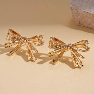 Elegant gold metallic pleated bow stud earrings on a textured beige background