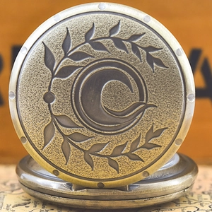 Close-up of vintage bronze pocket watch featuring embossed crescent moon and olive leaves