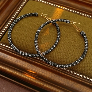 Detailed close-up of large round leather earrings with white letters on dark green fabric