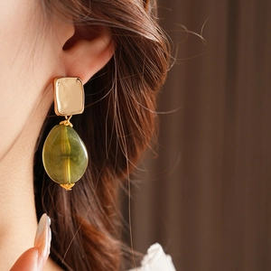 Detail shot of vintage green teardrop pendant earrings with gold square studs on model