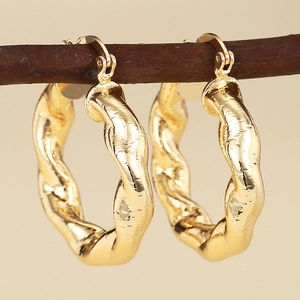 Goldene Creolen mit unregelmäßigem Spiraldesign und Textur auf einem Zweig