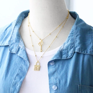 Close-up of double-layer gold necklace featuring crystal key and heart lock pendants