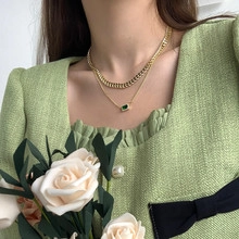 Detail shot of a minimalist gold snake chain and green square pendant necklace on a model