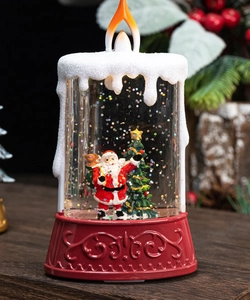 Close-up of a festive red water-filled LED candle with Santa and Christmas tree inside