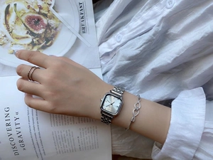 Detail view of a square silver stainless steel watch with matching bracelet and ring