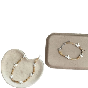 Bohemian beaded starfish necklace and bracelet set in beige on ceramic trays
