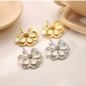 Close-up of gold and silver flower earrings on a minimalist ceramic background