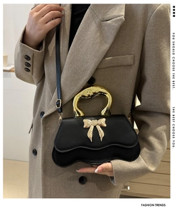Detail of black crossbody bag with wave design and golden heart bow metal handle
