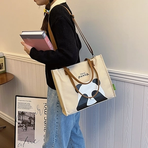 Minimalist canvas panda tote bag with brown handles, worn by a model in a cozy setting