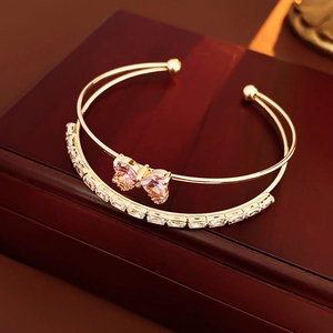 Macro shot of double-layered gold bracelet with pink zircon bow on wooden stand