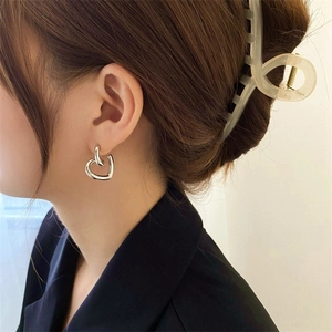 Minimalist silver heart-shaped stud earrings worn by a model in a side view portrait
