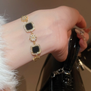 Détail d'un bracelet plaqué or 18k avec pierres noires carrées et breloques étoiles zircon