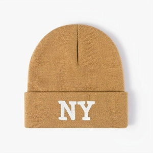 Close-up of white NY embroidery on a warm caramel-colored knitted beanie cap