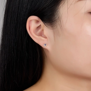 Close-up of elegant gold flower earring with purple gemstone and white zircon stones