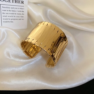 Detailed view of wide gold irregular metal cuff bracelet on white silk background