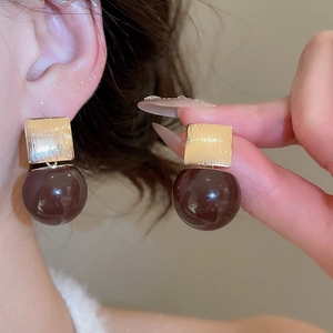 Macro detail of gold brushed square stud and glossy dark brown resin ball earrings
