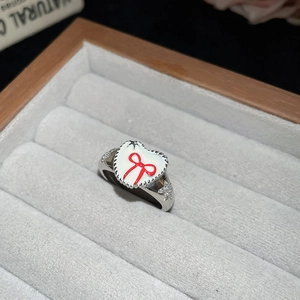 Close-up of a silver ring with a white enamel heart and a red bow in a jewelry box