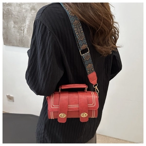 Detail of red cylinder bag with gold hardware and ethnic geometric strap on shoulder