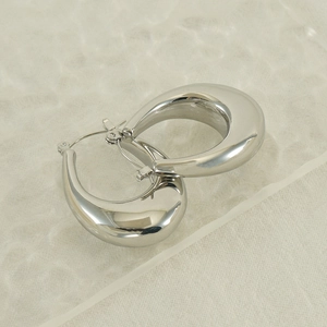 Detailed close-up of polished silver teardrop hoop earrings on textured fabric background