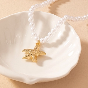 Macro detail of a pearl necklace with golden starfish pendant on a seashell plate