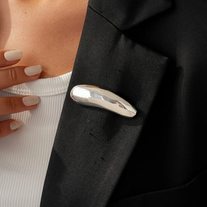 Close-up of a silver minimalist curved brooch pinned on a black blazer lapel with a mirror finish