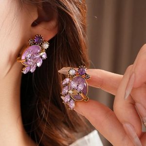 Detail of vintage gold earrings with purple crystals and pearl on model's ear