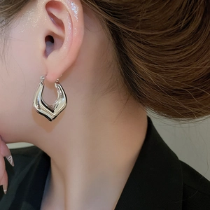 Macro shot of a minimalist silver U-shaped hoop earring worn on a model's earlobe