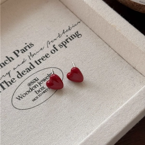 Close-up of red heart zircon stud earrings on a vintage beige fabric display tray