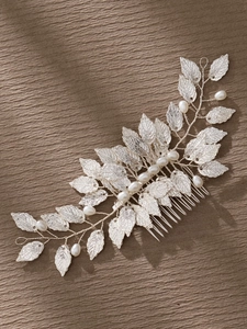 Detail of silver leaf bridal hair comb with elegant white pearls on brown fabric