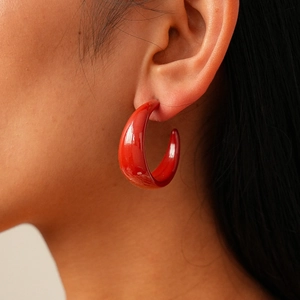 Close-up detail of a bright red thick C-shaped acrylic earring on a model ear