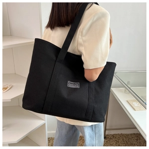 Detail view of large black canvas tote bag showing thick texture and FASHION woven label