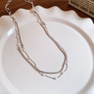 Close-up of double-layer silver necklace with pearls on a ruffled ceramic dish