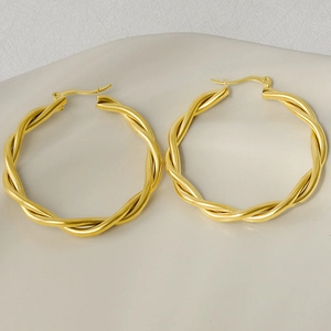 Detailed close-up of large golden twisted hoop earrings on ceramic display