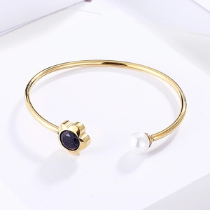 Detailed close-up of gold open bracelet with white pearl and blue crystal flower