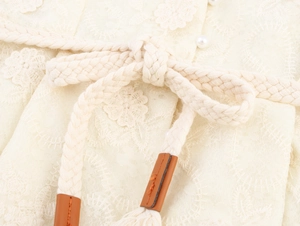 Détail d'une ceinture en coton tressé avec bouts en cuir et pompon sur robe dentelle