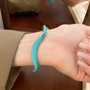 Detail of wavy turquoise resin bangle bracelet styled with a vintage brown blazer sleeve