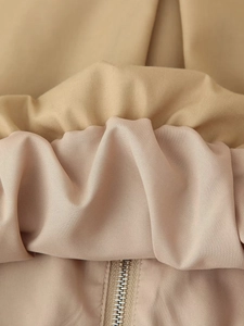 Détail d'une veste beige zippée montrant la texture du tissu et la fermeture éclair