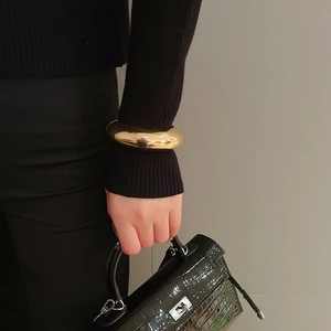 Close-up of minimalist gold cuff bracelet worn over black knit sleeve with a bag