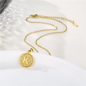 Macro shot of gold circular necklace pendant featuring an engraved letter K on a clean surface