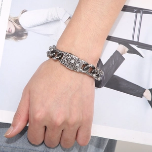 Close-up of punk style men's silver skull chain bracelet worn on wrist over a magazine