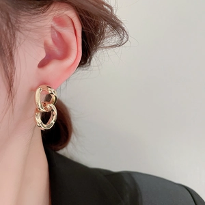 Close-up of elegant gold double-loop earrings worn by a model in soft lighting
