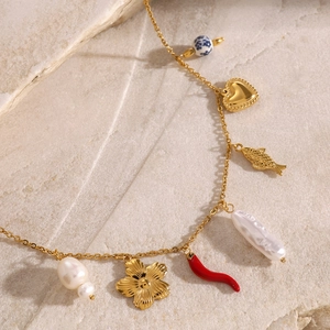 Golden stainless steel necklace with baroque pearl, heart, and floral charms on a stone surface