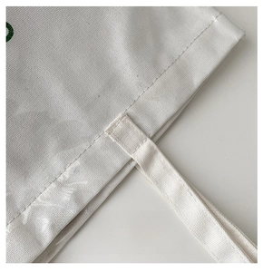 Detailed close-up of precise stitching and durable canvas strap on a white tote bag