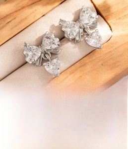 Macro shot of silver bow earring with three heart-shaped zircons and a swinging pendant